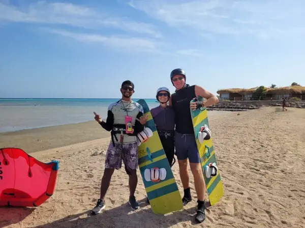 Instructor with two guests holding kiteboards on the beach