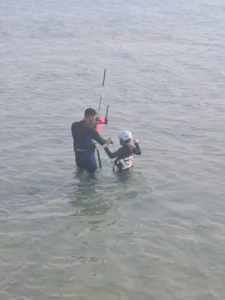 Instructor teaching a child to kite in shallow water